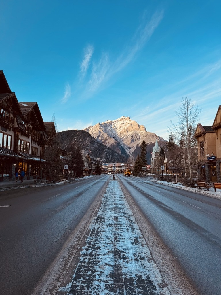 Looking down an icy Banff Avenue on a clear winter morning, Cascade Mountain lit up at the end of the street.