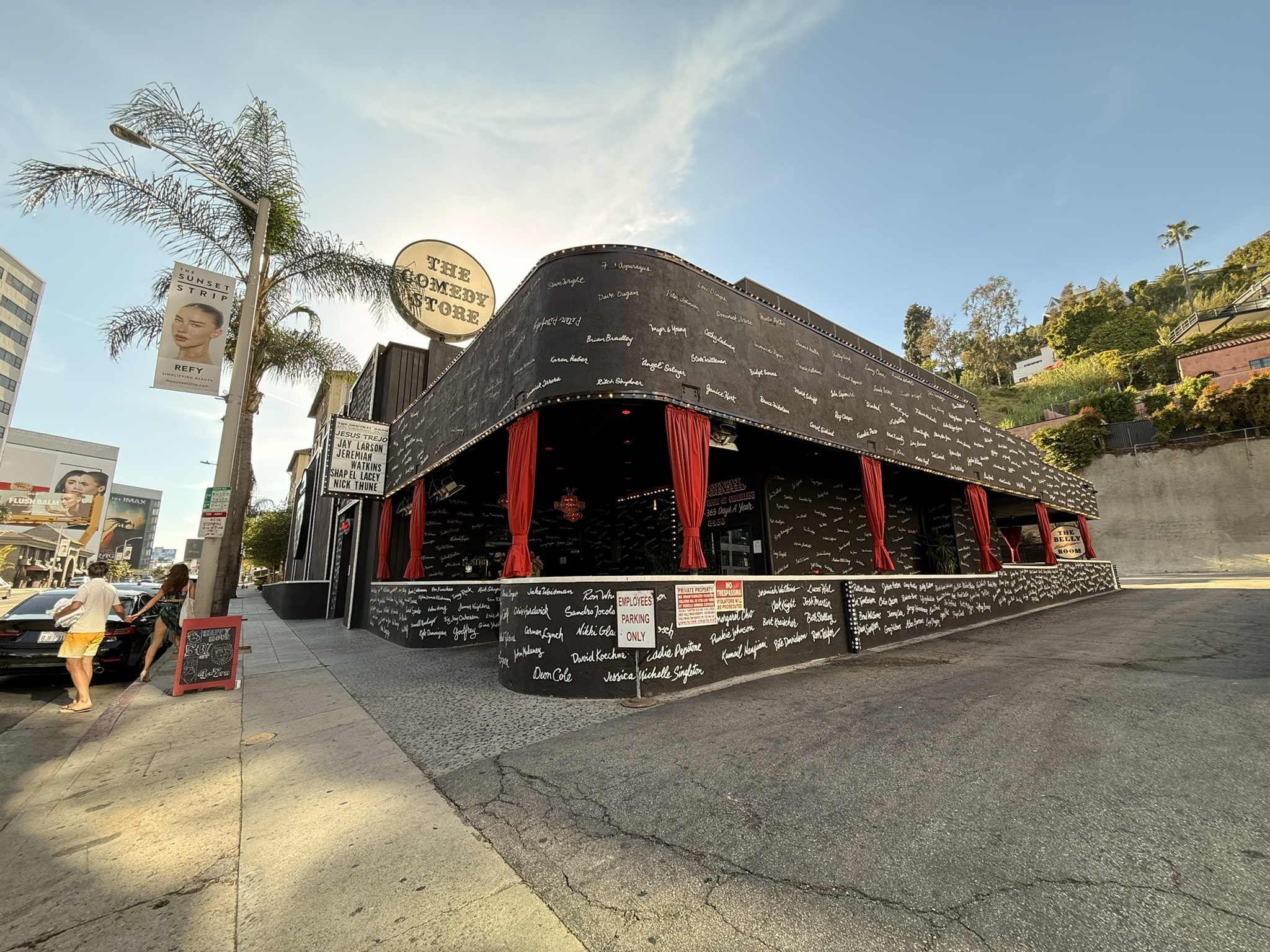 The Comedy Store on the Sunset Strip, its curved black walls covered in comedians' names in white script, red curtains in the windows.