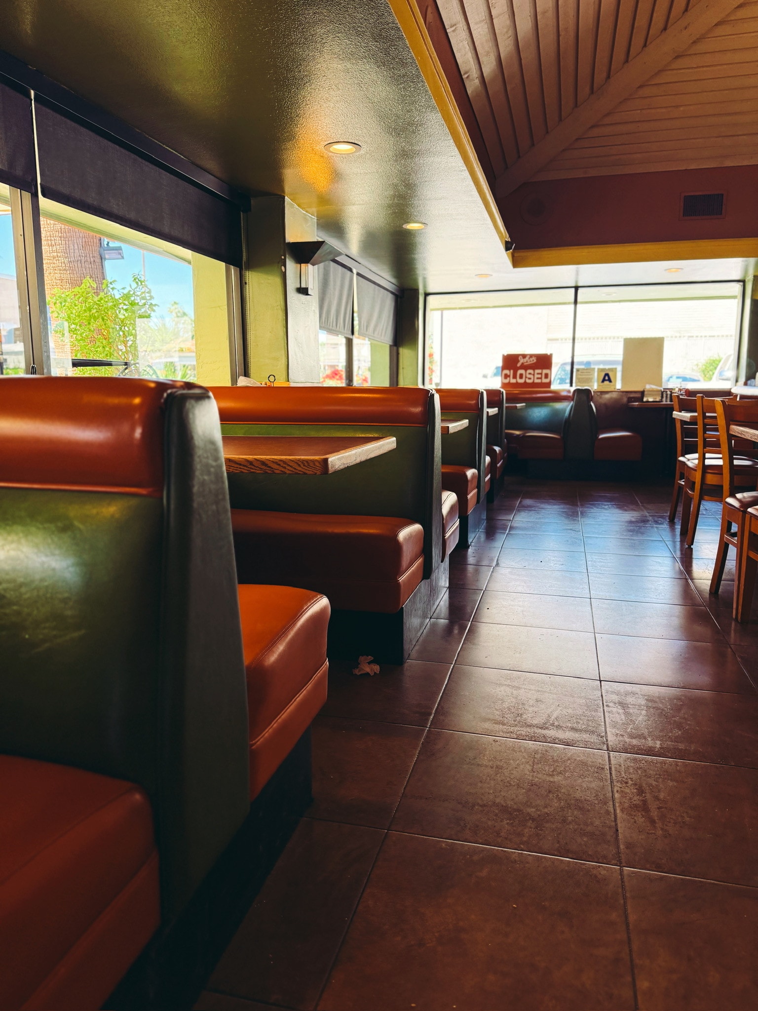 Empty diner with rows of orange and green vinyl booths, sun pouring through the windows and a Closed sign by the door.