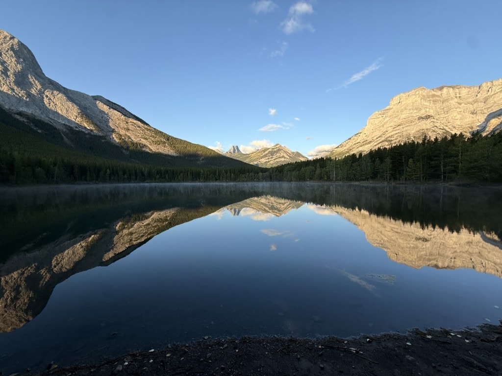Early sun lighting two limestone mountains, both reflected perfectly in a calm pond with a thin layer of mist.